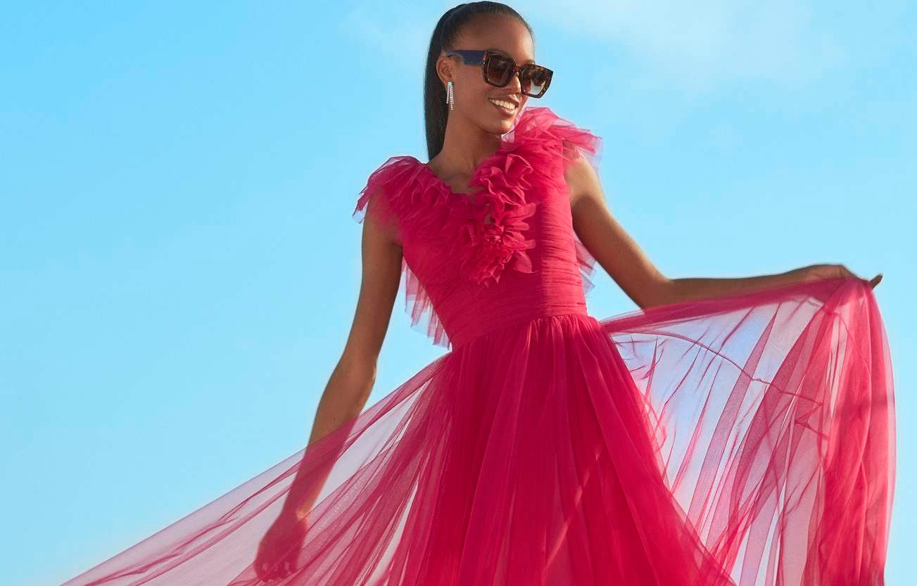 Mujer luciendo un vestido fucsia de invitada perfecta sonriendo con el cielo azul de fondo