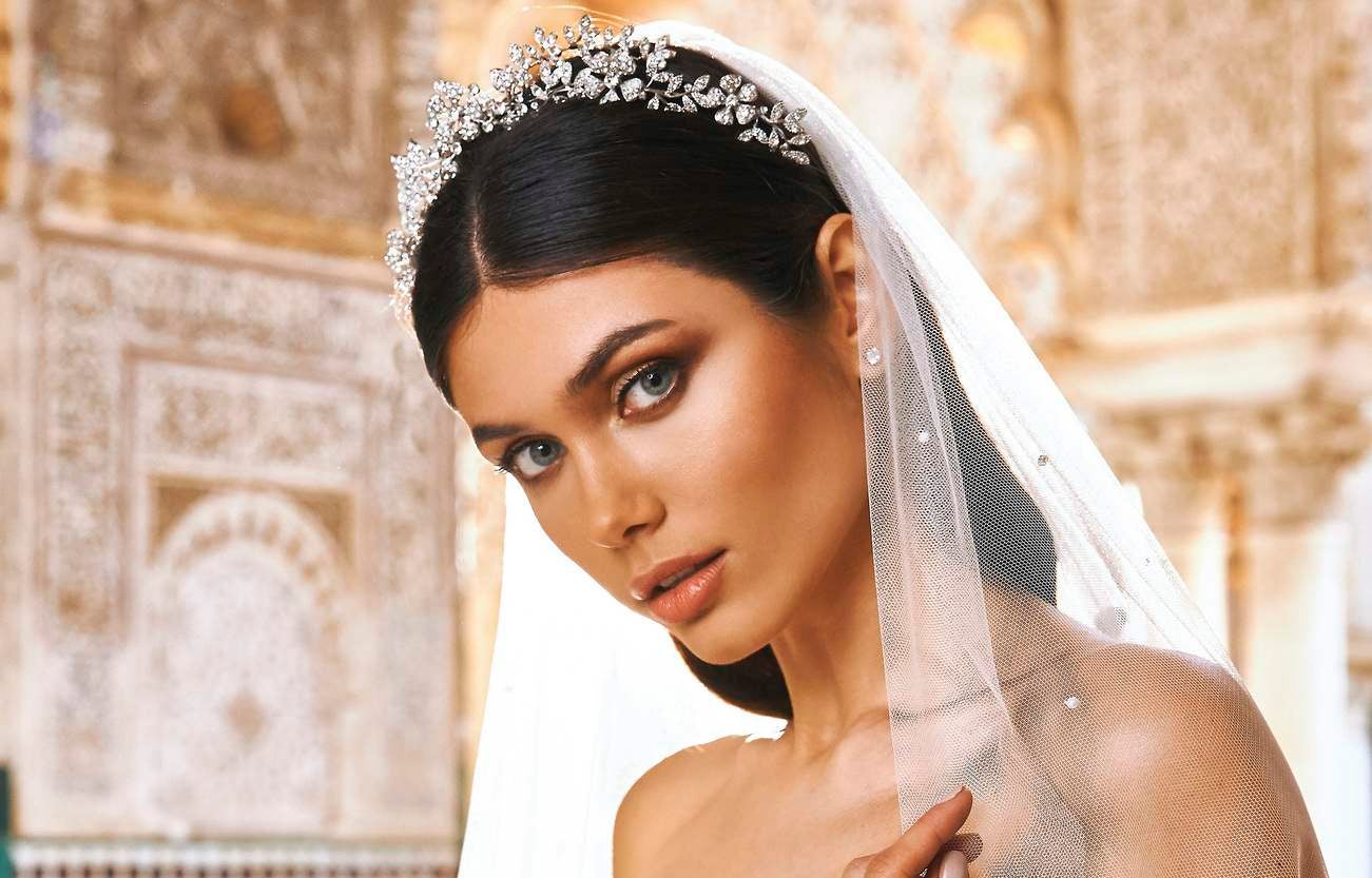 Noiva usando um véu longo preso num tiara com detalhes florais prateados combinado com uma make simples e luminosa