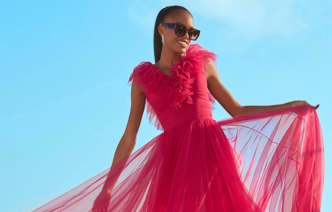 Convidada usando um vestido longo vermelho conjugado com uns óculos de sol e uns brincos longos