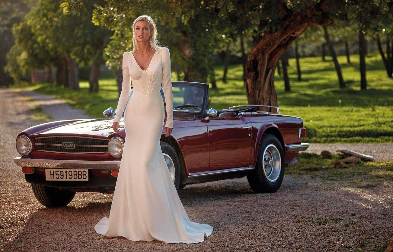 Mujer a plena luz del día con el cielo azul y el sol de fondo con manga larga en su vestido de novia