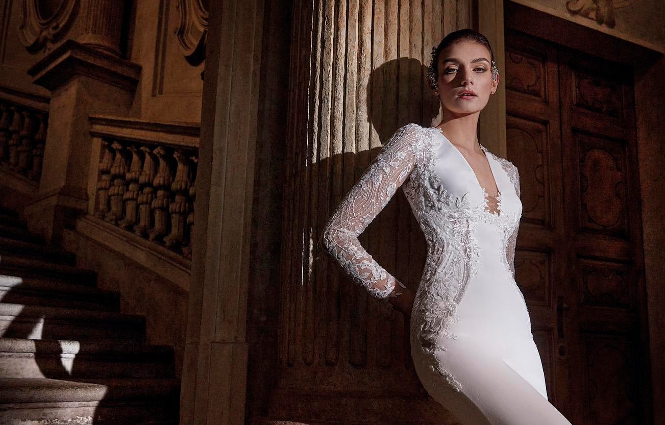Mujer apoyada sobre una columna con el pelo recogido y un vestido de novia con escote en pico.