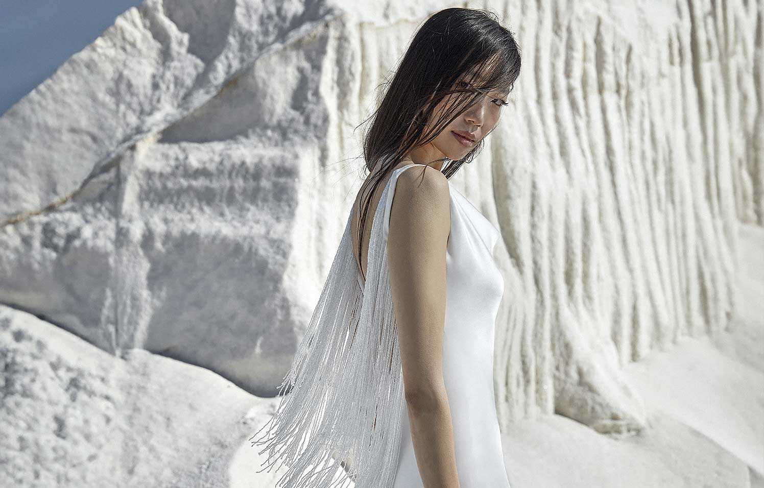Mujer mirando de perfil con vestido de novia blanco de tirantes.