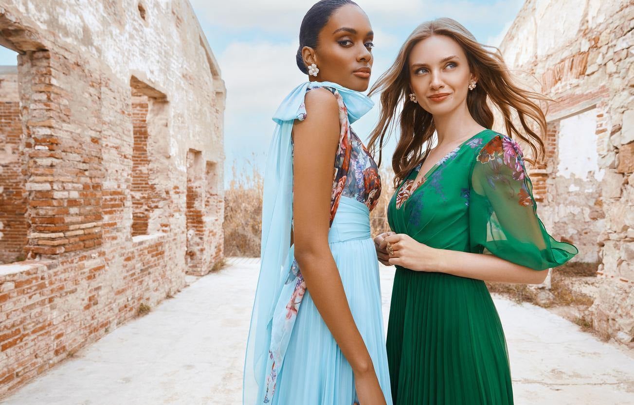 Damas de honor posam com vestidos fluidos azul e verde com motivos florais em ambiente de casamento campo