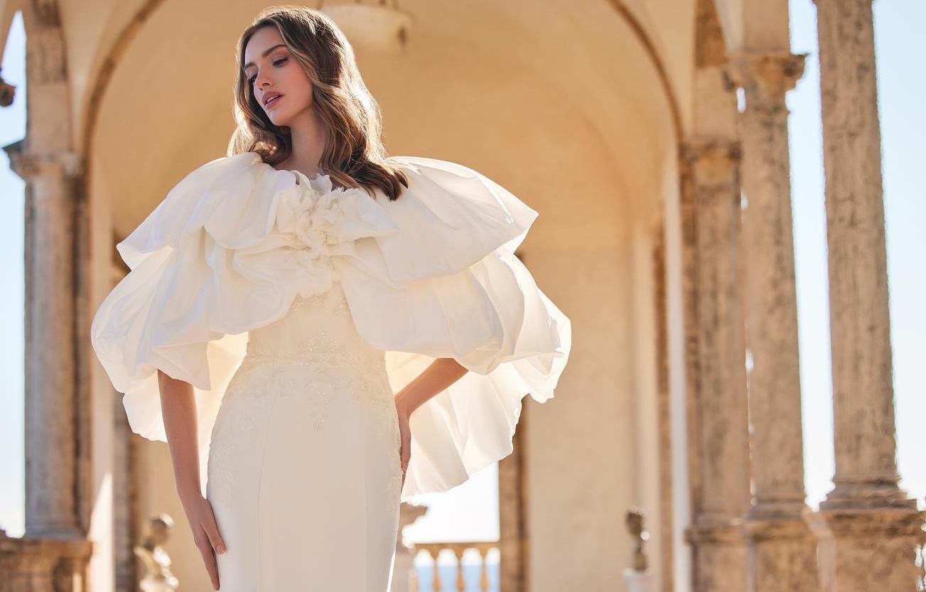 Modelo usa vestido de noiva tendência com capa volumosa sobre corte de sereia simples e penteado de cabelos soltos