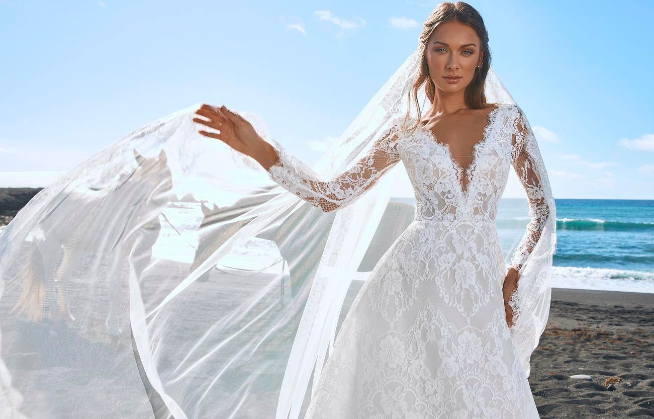 Panna młoda w długiej koronkowej sukni ślubnej z głębokim dekoltem unosząca w prawej dłoni długi rozwiany welon