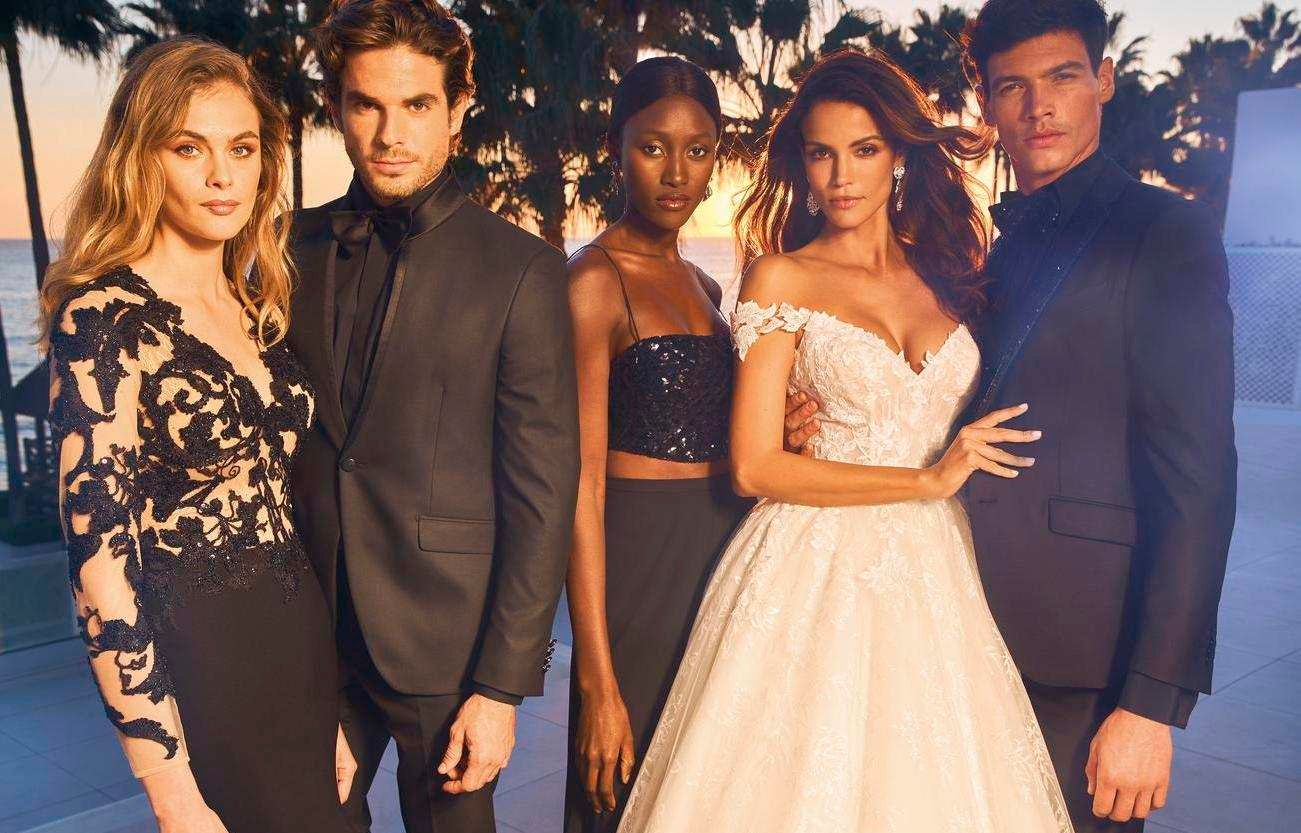 Panna młoda ubrana w białą suknię ślubną oraz pan młody i przyjaciele ubrani na czarno pozujący do wspólnego zdjęcia