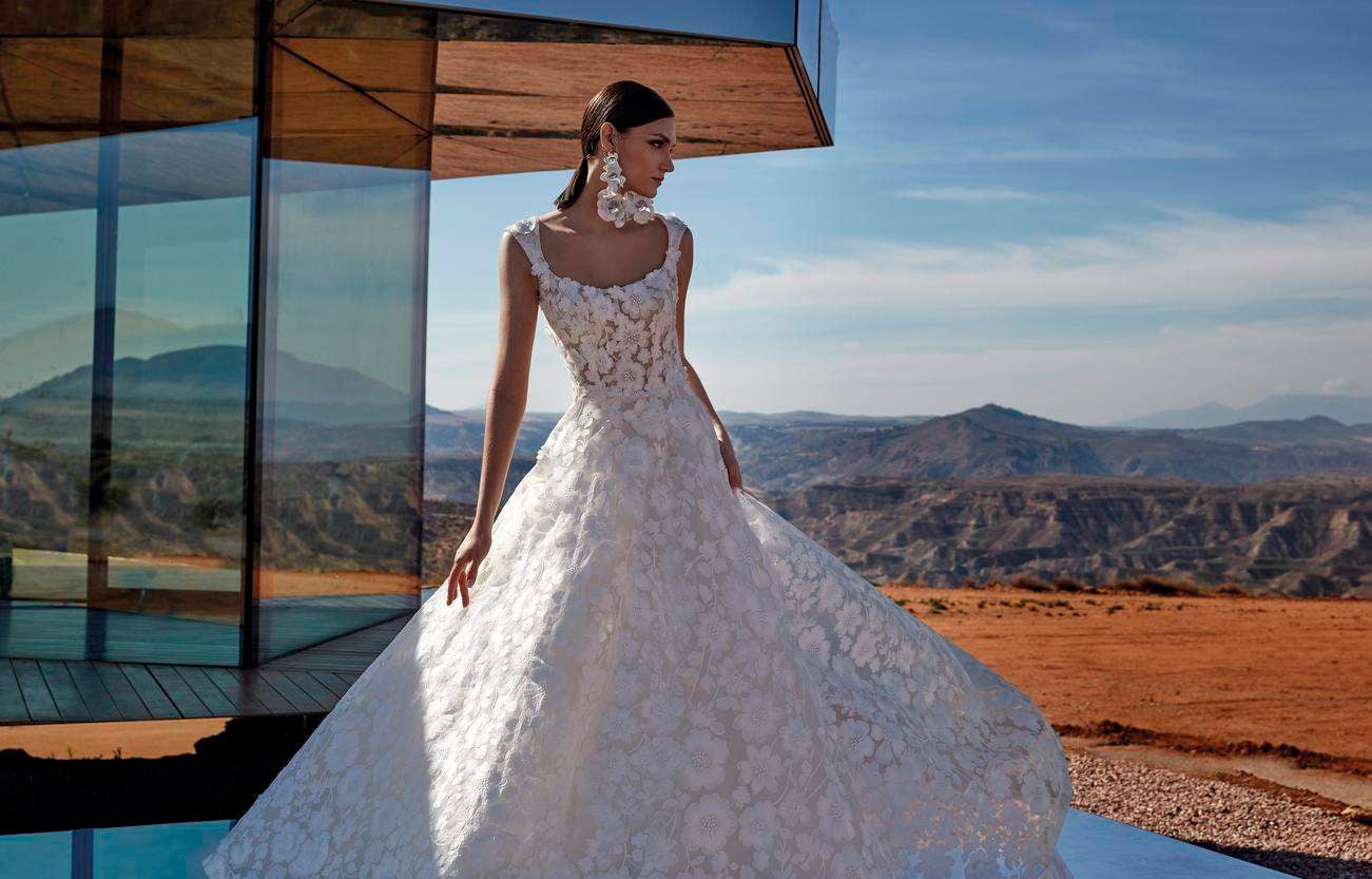 Panna młoda ubrana w kwiecistą suknię ślubną w stylu księżniczka i długie kwieciste kolczyki pasujące do gładkiego uczesania