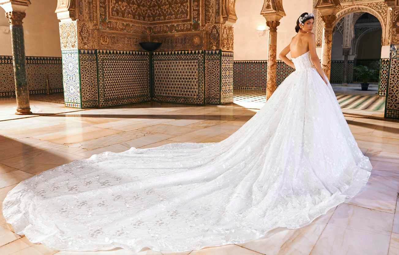 Panna młoda w sukni ślubnej w stylu księżniczka z długim trenem na tle eleganckiej przestrzeni 