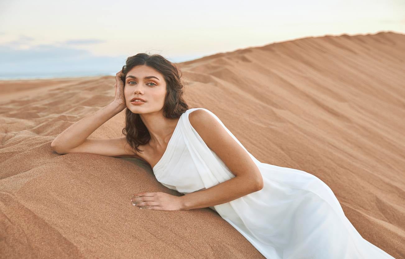 Une élégante femme vêtue d'une robe de mariée style empire, se prélassant gracieusement sur le sable fin.