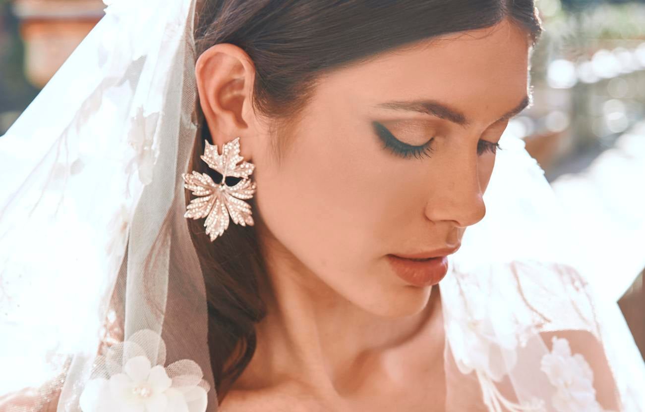 Twarz panny młodej spoglądającej w dół ubrana w welon ślubny oraz złote kolczyki ślubne w formie liścia ze zdobieniami