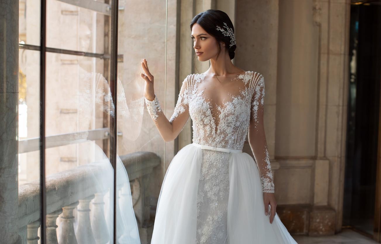 Panna młoda w długiej sukni ślubnej i eleganckim upięciem wyglądająca przez szybę okna