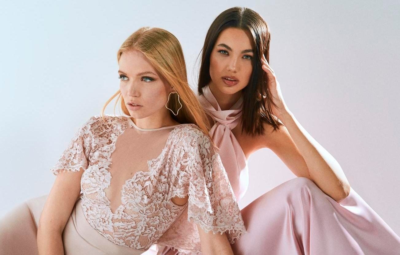 Frau mit hellen Haaren in rosanem Kleid mit Spitzenapplikationen und Frau mit dunklen Haaren in langem Kleid aus Seide