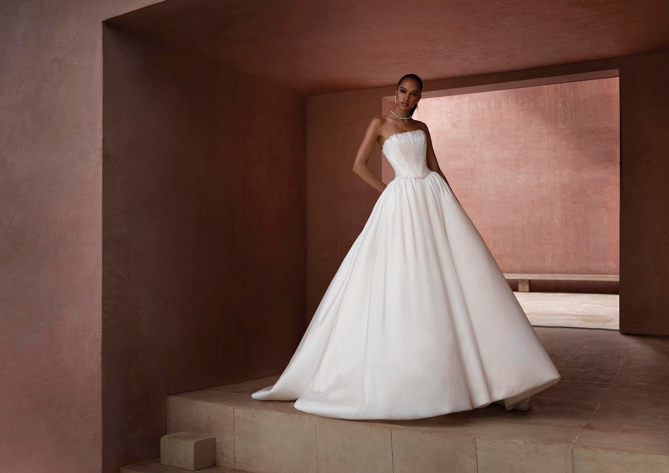 Une femme élégante, vêtue d'une robe de mariée princesse se dresse sur une marche.