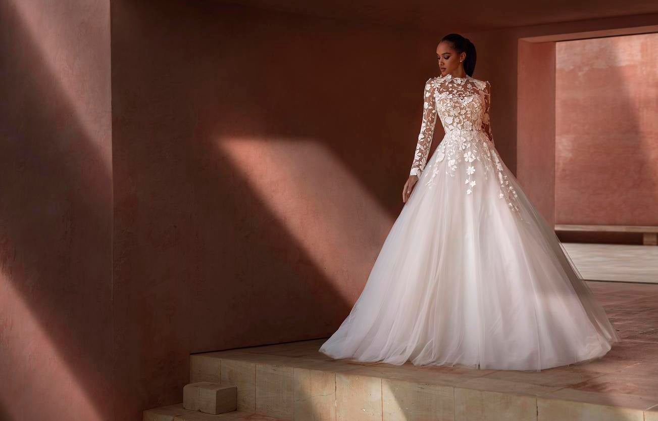 Ciemnoskóra Panna młoda prezentuje jasno różową suknię ślubną z bogatym zdobieniem na górze i długimi rękawami