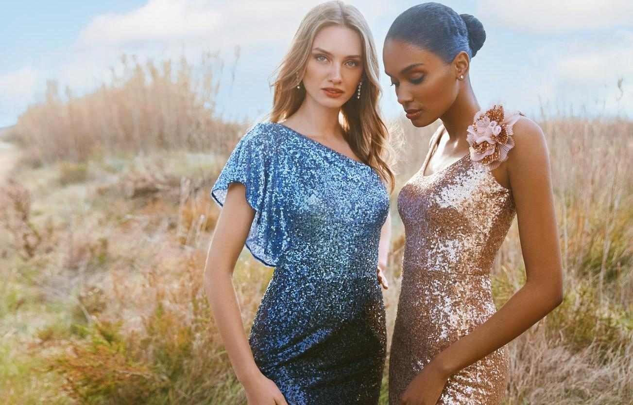 Dwie kobiety stojące w plenerze ubrane w eleganckie suknie na przyjęcie weselne