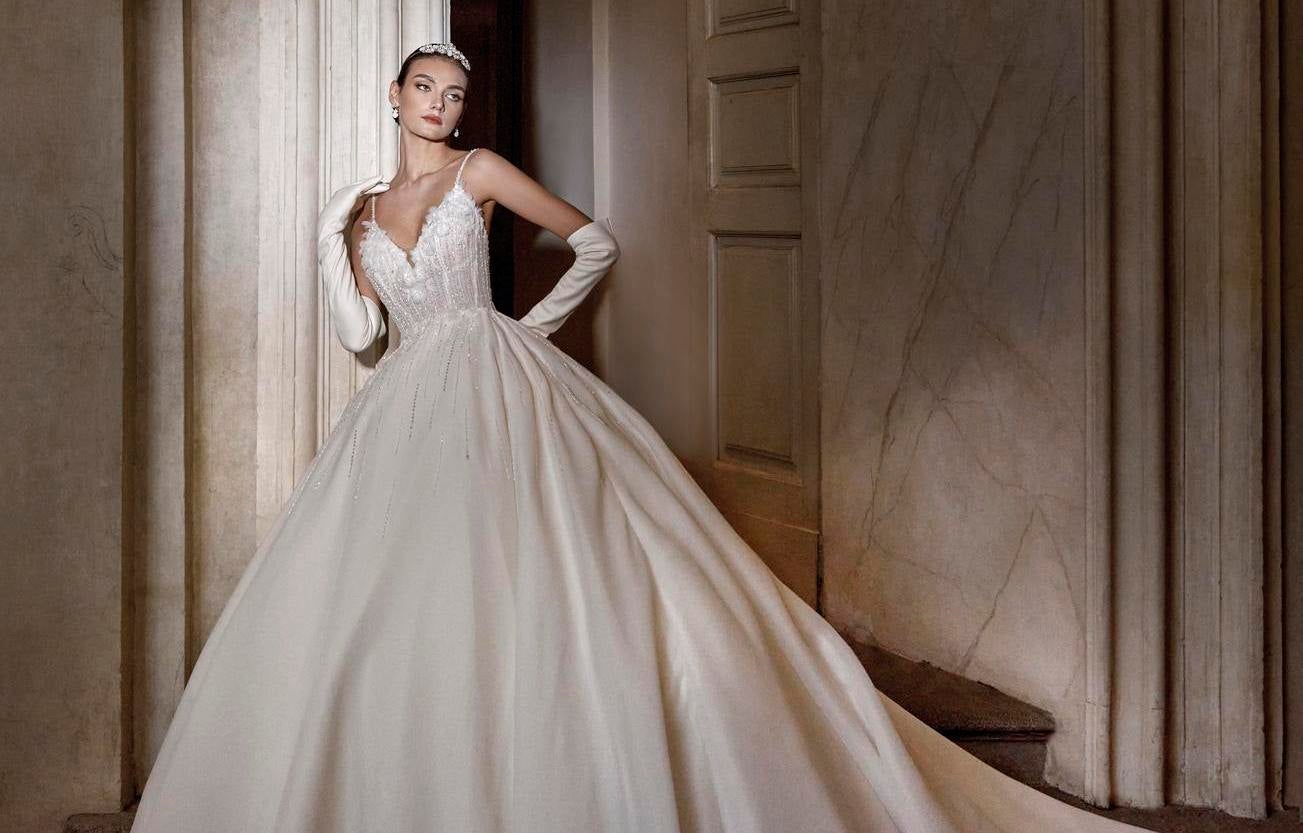 Sposa con capelli raccolti che indossa un lungo abito stile principessa con svollo a V e spalline sottili.
