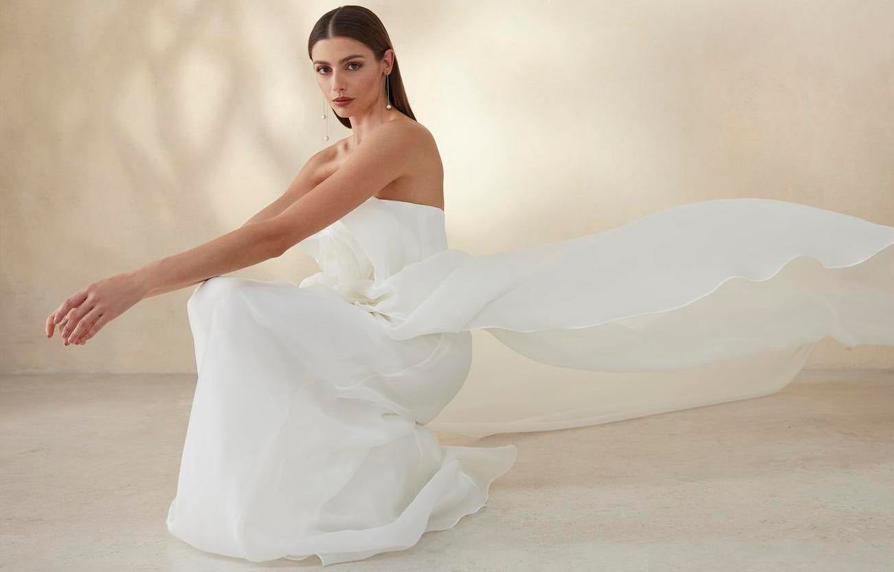 Modella con capelli sciolti che indossa un abito da sposa lungo senza spalline con strascico