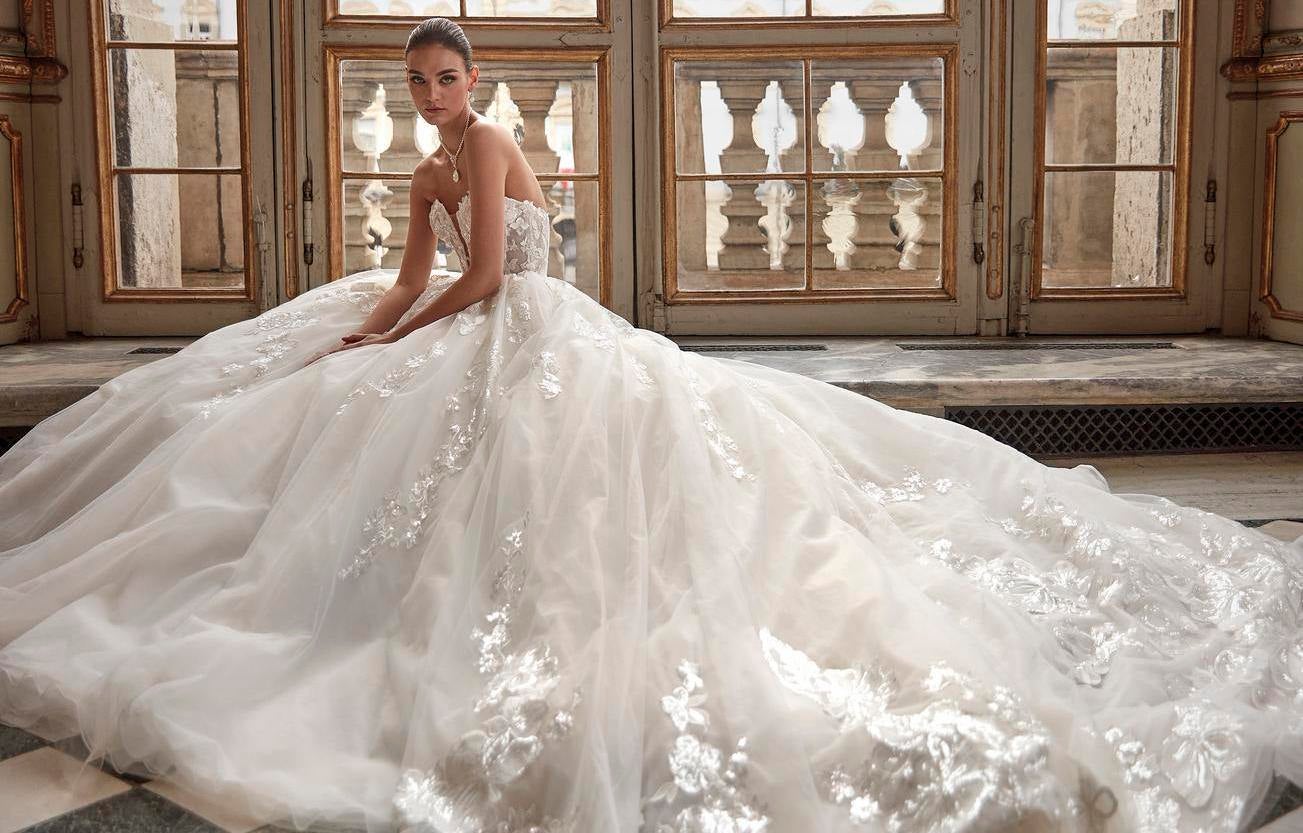 Noiva com vestido princesa de renda cai cai e decote coração sem mangas com bijutaria sentada no chão de um espaço clássico