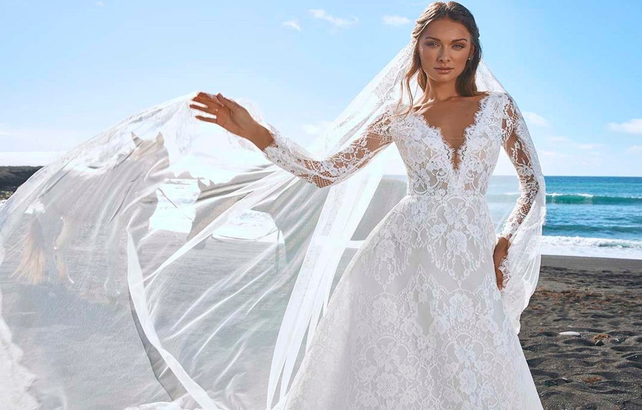 Une belle mariée sur la plage, vêtue d'une robe de mariée à manches longues en dentelle et d'un voile en dentelle