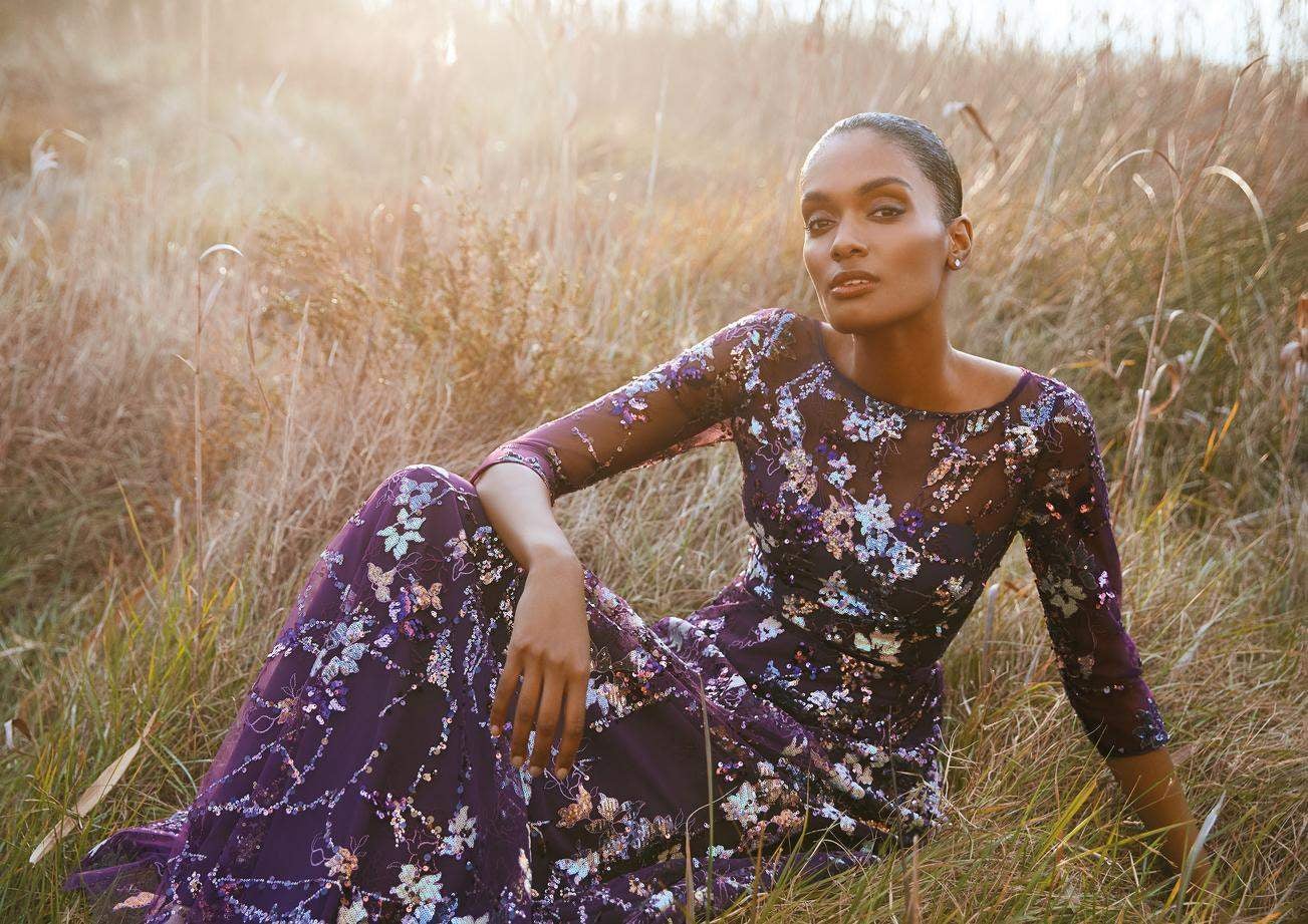 La mère de la mariée, vêtue d'une robe violette à motifs floraux et à manches longues, assise dans les hautes herbes
