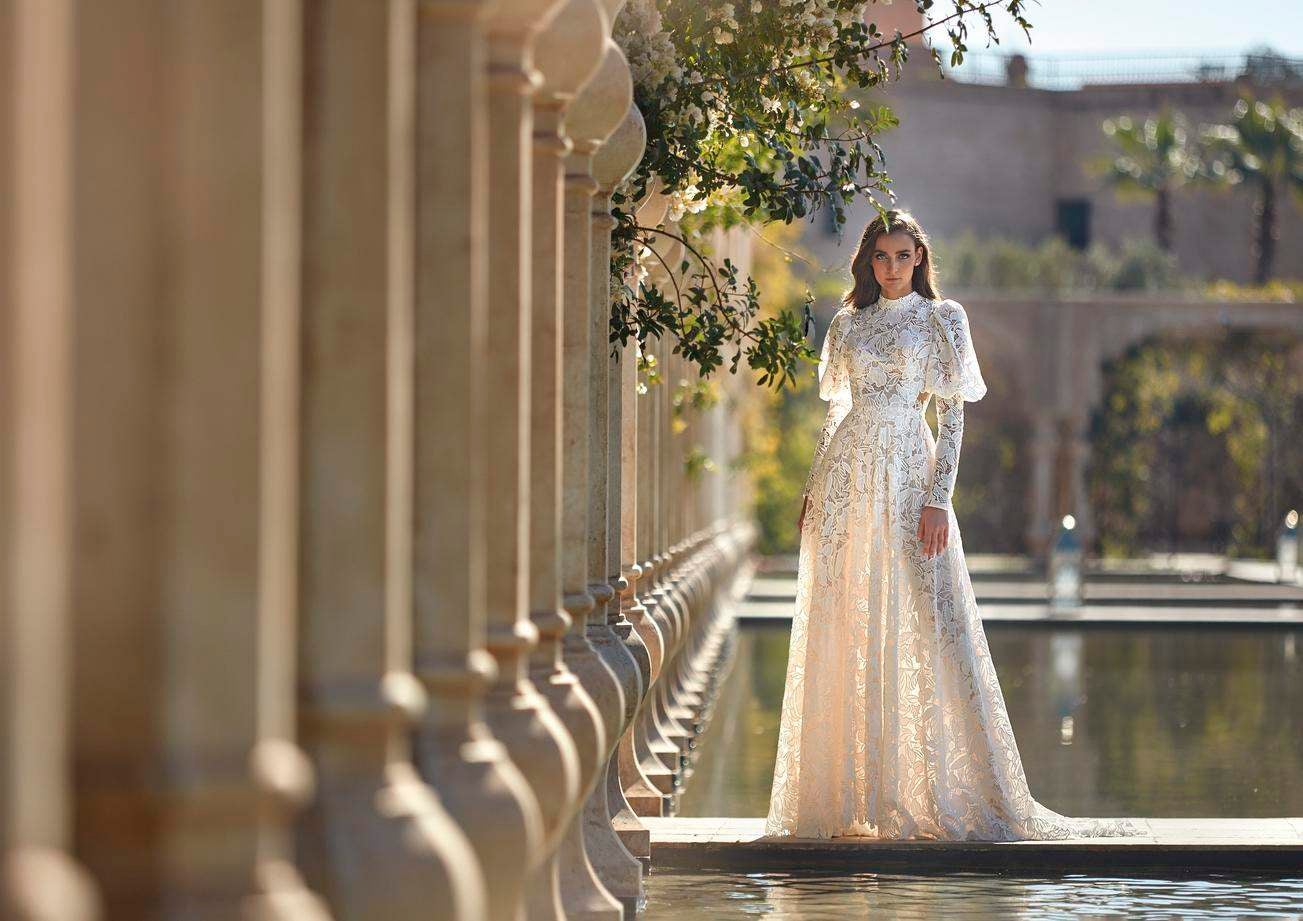 Une ravissante mariée portant une robe de mariée en dentelle avec un col haut et de longues manches bouffantes.