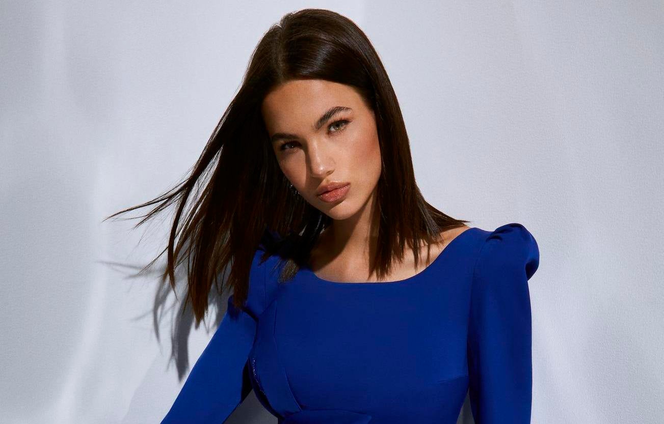   Brunette with loose hair wearing a blue evening gown with long sleeves, looking straight ahead
