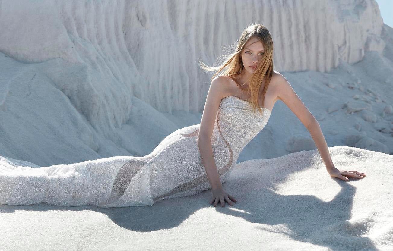 Blonde women with loose hair, wearing a strapless wedding dress, sitting on a white rock outside
