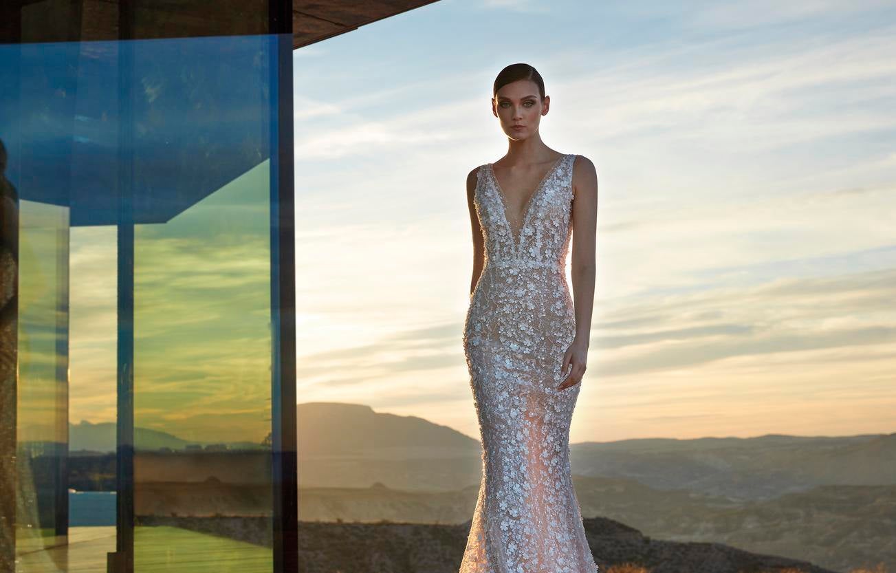 Woman wearing a mermaid wedding dress with beading and a plunging V-neck, standing outside with mountains on the background