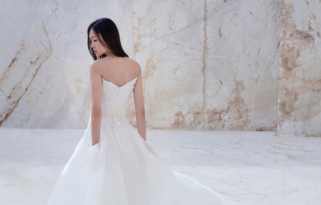 Brunette wearing an A-line strapless wedding gown in lightweight silk organza, standing outside against a white background