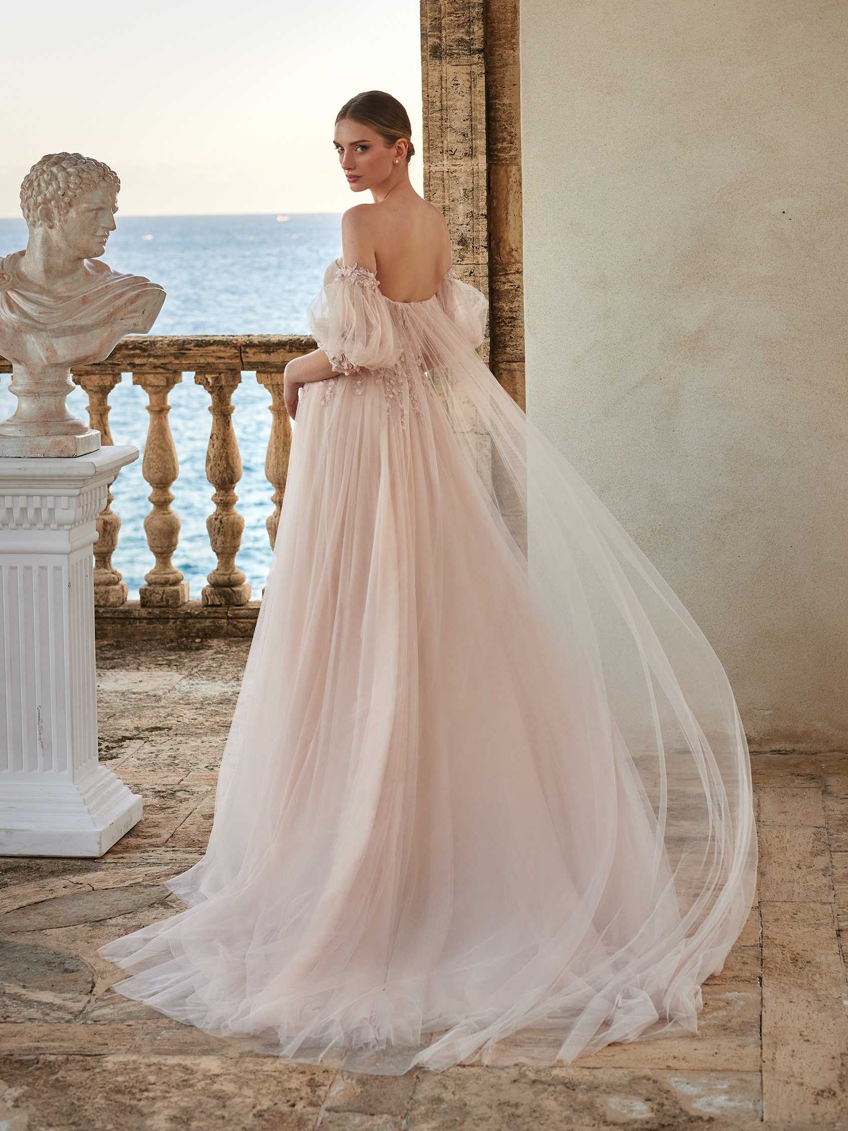 Mujer mirando de espaldas con vestido de novia de invierno y un recogido con el mar de fondo.