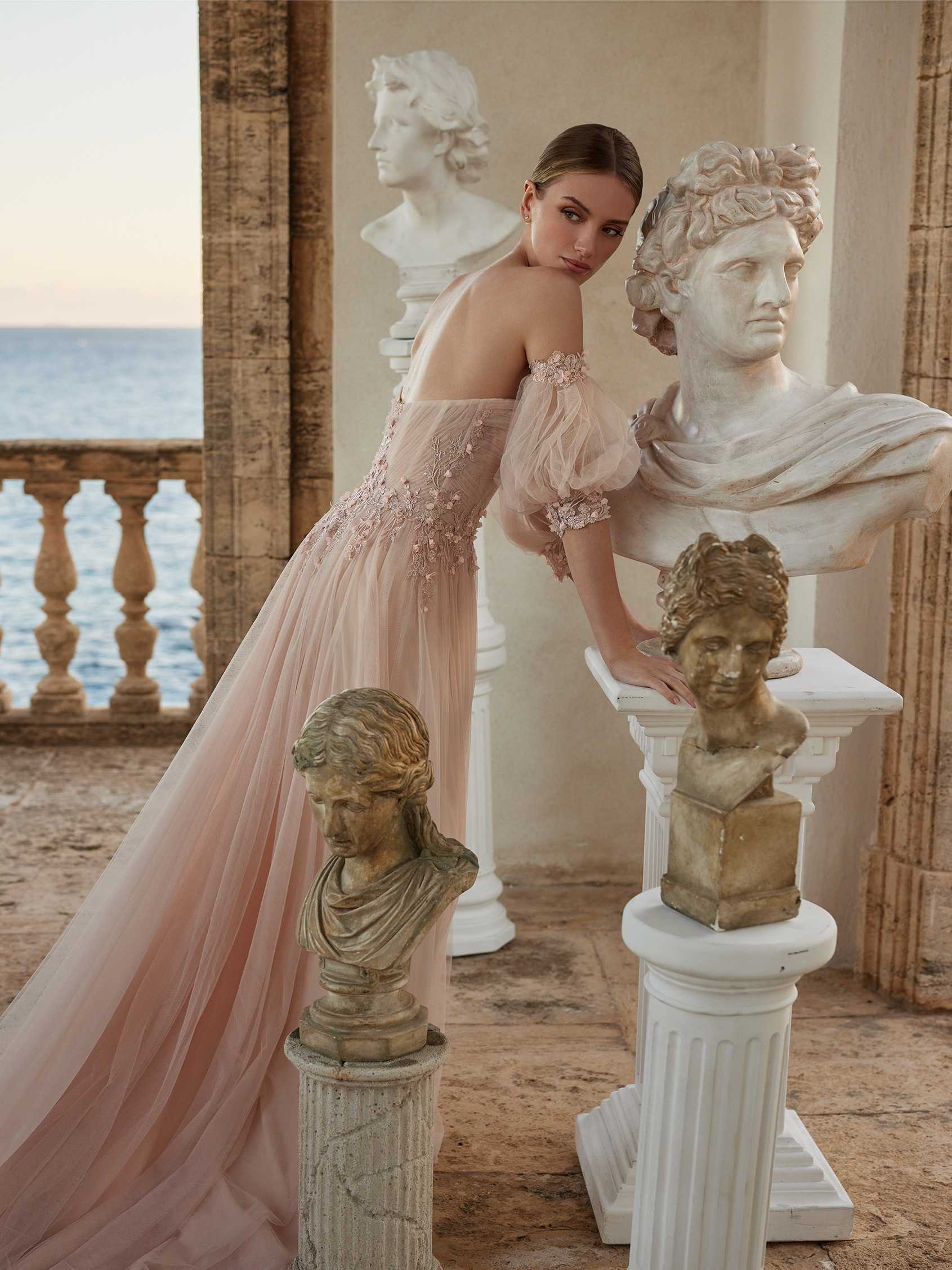 Mujer apoyada sobre unas esculturas con un vestido de novia rosa con mangas abullonadas.