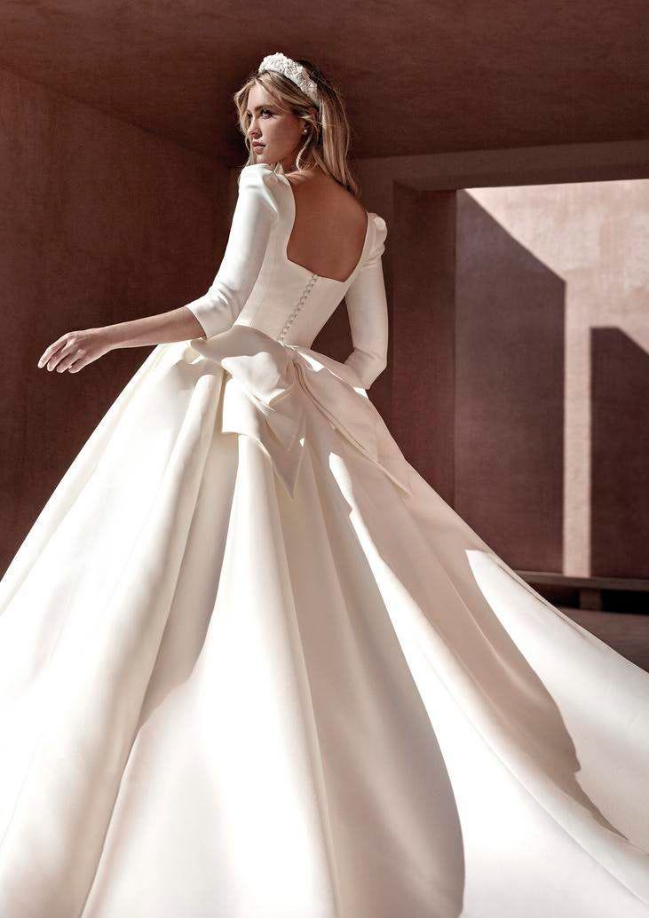 Une jeune femme habill&eacute;e d'une robe de mari&eacute;e princesse simple dot&eacute;e de manches 3/4 et d'une d&eacute;coupe carr&eacute;e dans le dos. 