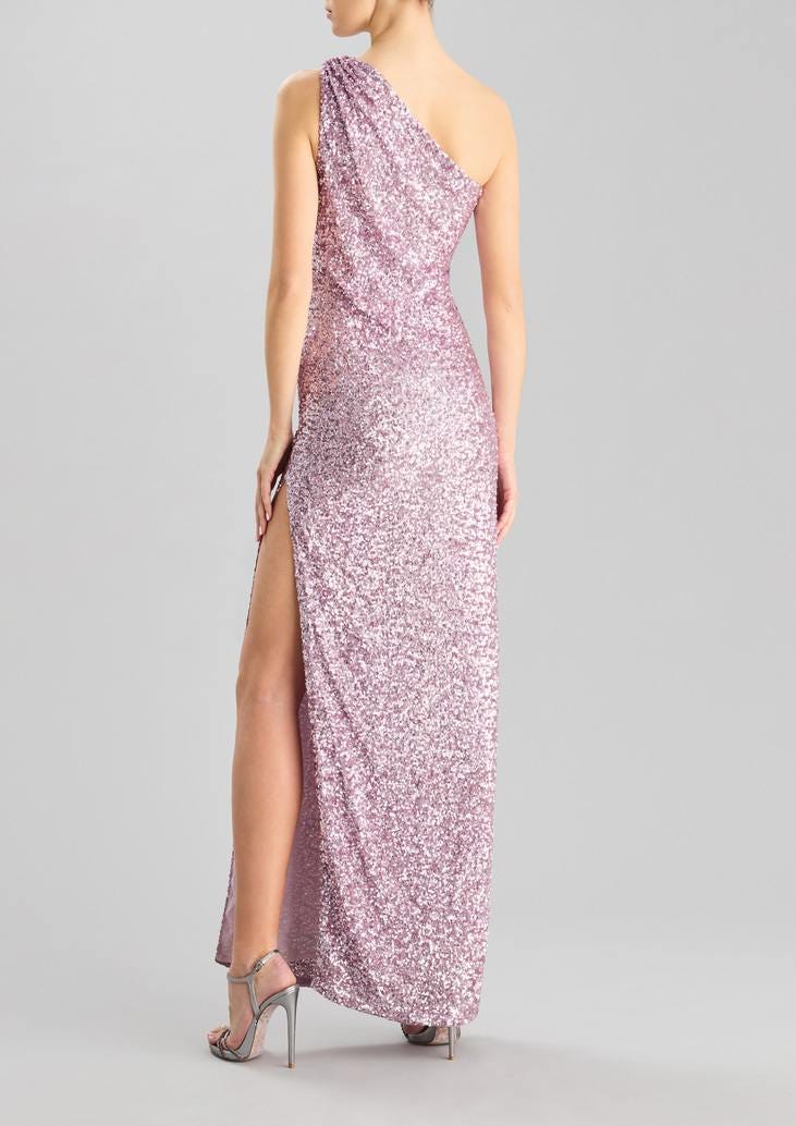 Convidada de casamento posa de costas com sapatos altos prateados e um vestido longo rosa brilhante, com racha, lantejoulas e costas descobertas 