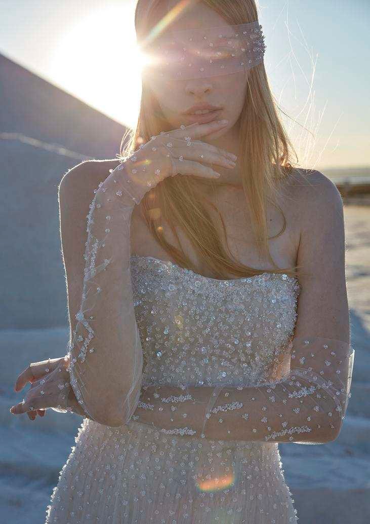 Une jeune femme arborant une robe de mari&eacute;e bustier &agrave; strass, agr&eacute;ment&eacute;e de gants en tulle, eux aussi, recouverts de strass.
