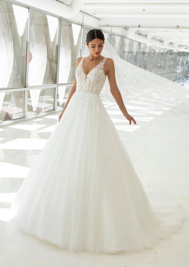 Panna młoda w długiej tiulowej sukni ślubnej w stylu księżniczka z długim welonem doczepionym do gładkiego upięcia