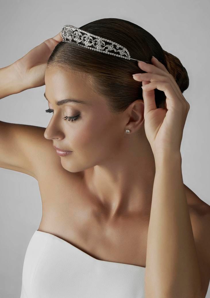 Portrait d’une mariée dotée de courtes boucles d’oreilles, posant son diadème fin et argenté sur ses cheveux