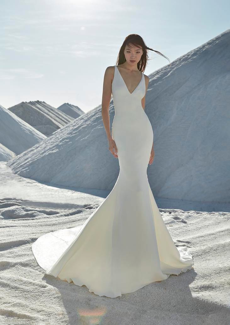 Abito da Sposa con Scollo a V Modella che indossa un abito da sposa bianco, semplice ed elegante a sirena con scollatura a V.