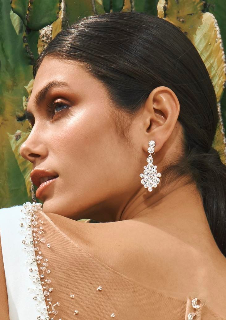 Pendientes para novia Mujer mostrando sus pendientes de novia donde se ven sus hombros con un vestido de novia con pedrería