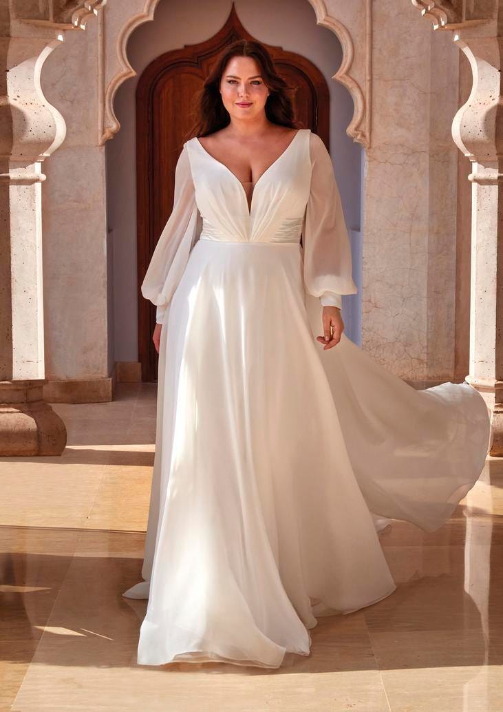 Modella che indossa un abito da sposa curvy semplice con maniche lunghe e scollo a V.