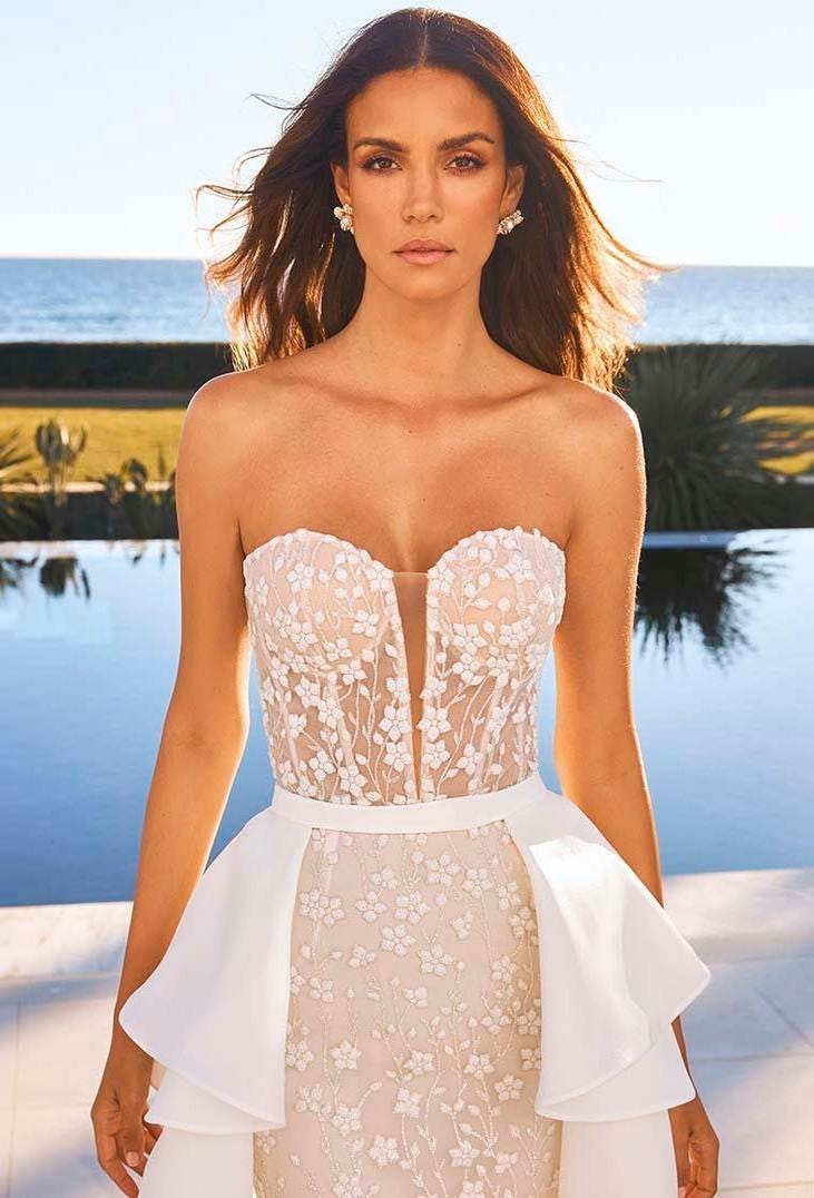 Une robe de mari&eacute;e sans bretelles en dentelle avec un d&eacute;collet&eacute; plongeant et une surjupe blanche amovible.
