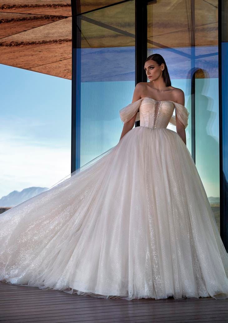 Modella che indossa un abito da sposa stile principessa con gonna ampia e voluminosa e spalline cadenti.
