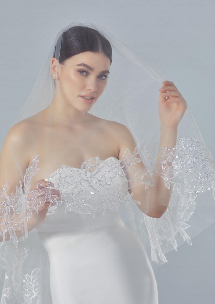 Modella in primo piano che indossa un abito da sposa semplice senza spalline e un velo in tulle ricamato sui bordi.