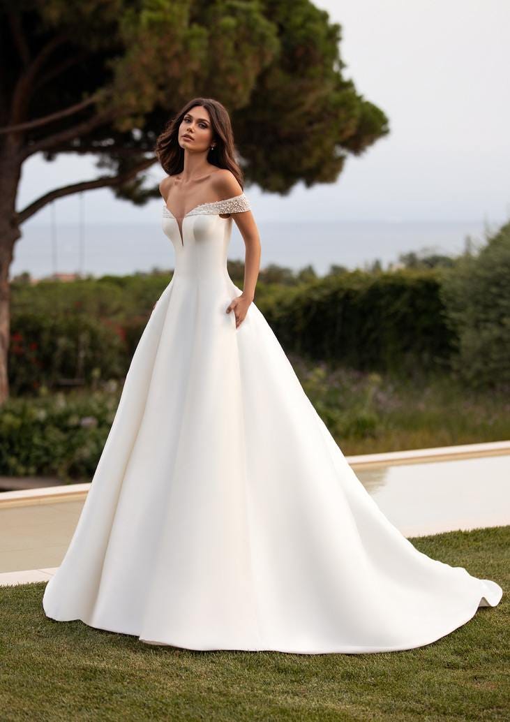 Noiva de cabelos longos com um vestido linha A branco e simples com umas alças adornadas com pérolas