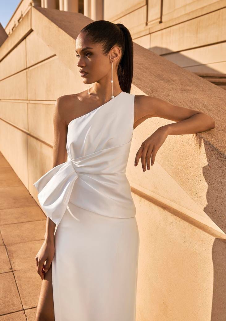 Noiva usando um vestido longo com fenda, de uma só alça conjugado com um rabo de cavalo e uns brincos com pérolas