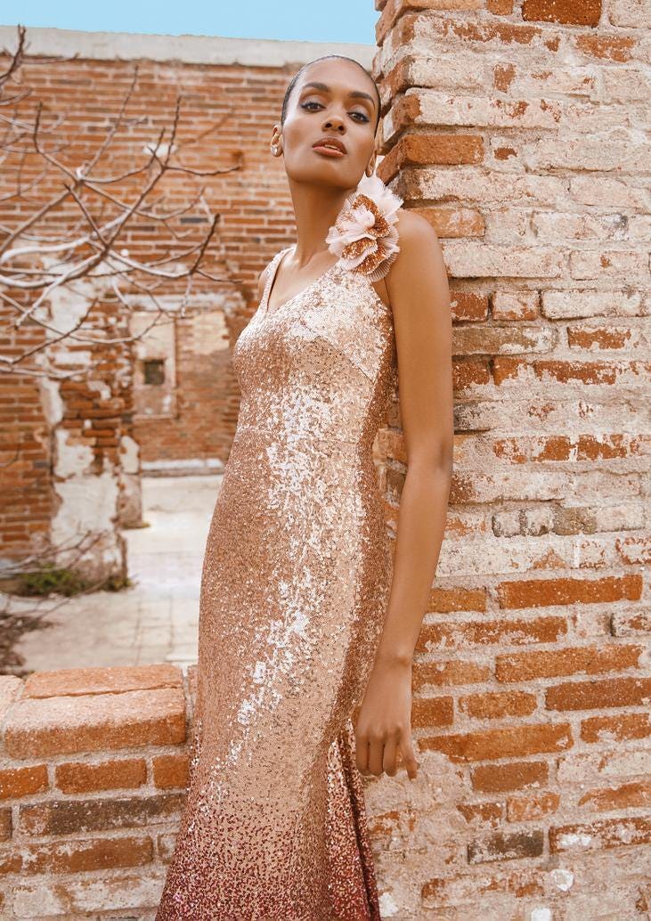 Convidada posa com vestido de dama de honor longo simples dourado de lantejoulas com aplicação de flor e penteado preso com brincos 