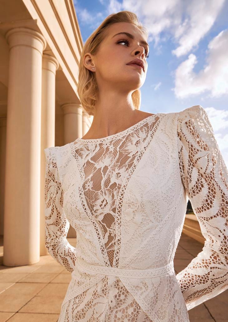 Blonde Frau in weißem Brautkleid aus durchsichtiger Spitze in die Ferne schauend 