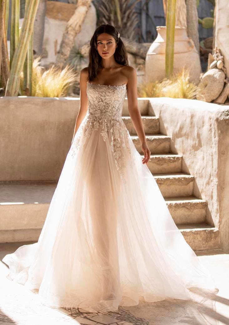 Panna młoda prezentująca suknię ślubną w kolorze pudrowego różu bez ramiączek z delikatnym wzorem kwiatowym