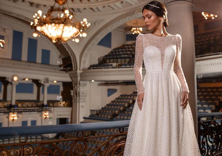 Kobieta w sukni ślubnej na tle sali koncertowej lub teatru spoglądająca w prawą stronę