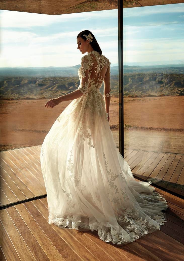 Mujer de pefil con un vestido de novia con transparencias y un tocado para pelo suelto y al fondo las monta&ntilde;as y el cielo