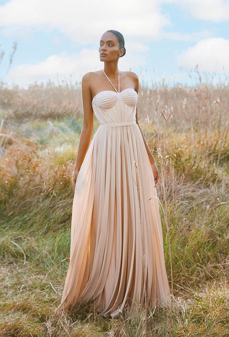 Une femme &eacute;l&eacute;gante dans une longue robe fluide rose se tient gracieusement dans un champ verdoyant.